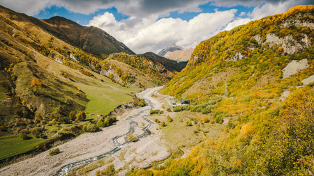 Panoramic autumn view of a winding river in the Georgian mountains. Vibrant foliage, rugged hills,...