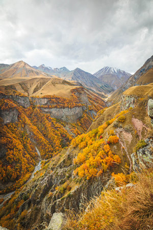 Dramatic autumn mountain scenery in Gudauri, Georgia, with golden forests covering deep valleys and...