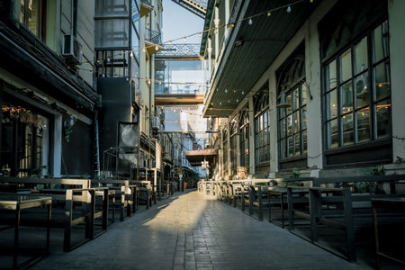 Narrow alley with empty outdoor cafes and hanging lights in Tbilisi, Georgia, illuminated by soft morning sunlight, evoking a calm and cozy urban atmosphereの写真素材