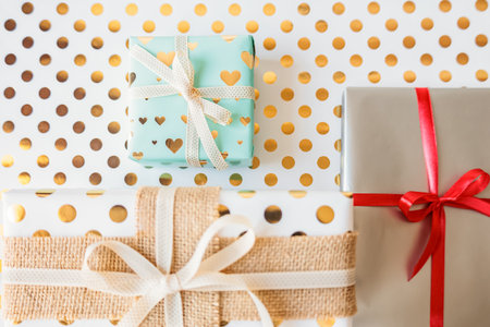 Beautifully wrapped gift boxes with ribbons on festive golden polka dot background. Bright and...