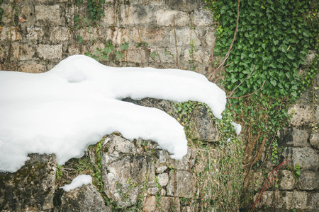 Aged stone structures in Kutaisi, Georgia with fresh snow and green ivy in winter. A symbolic view of the passage of time and nature reclaiming historyの写真素材