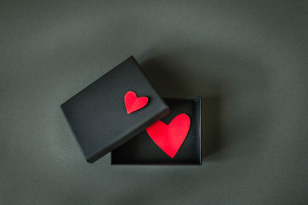 Minimalistic Valentine's Day composition with black gift box and red paper heart on dark background....