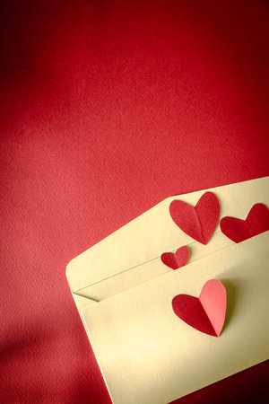 Love letter concept with paper red hearts flying out of cream envelopes on red background. Minimal...