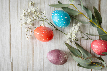 Colorful pastel Easter eggs with delicate white flowers and eucalyptus arranged on one side of...