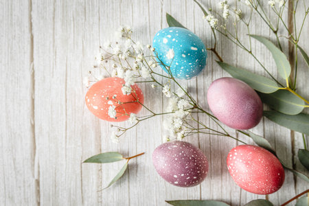 Colorful pastel Easter eggs with eucalyptus branches and delicate white flowers on rustic wooden...