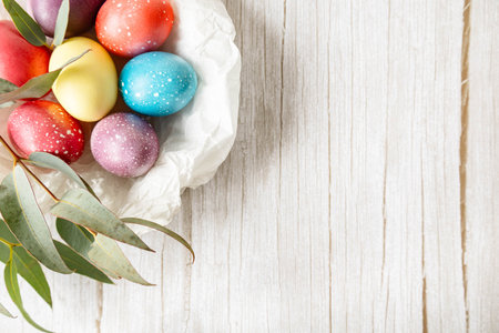Colorful pastel Easter eggs in white paper nest on rustic wooden background with copy space. Soft...