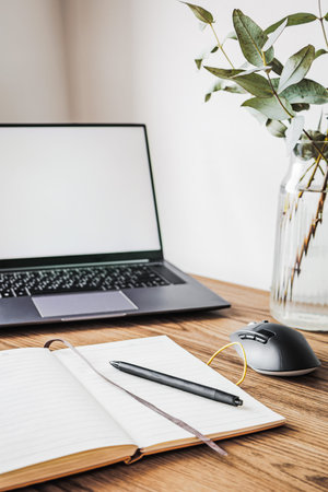 Modern home office workspace with laptop mockup screen, open notebook with pen, computer mouse and...