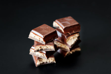 Close-up of dark chocolate candy pieces with light filling on a black background, rich moody dessert photo with glossy texture and copy space