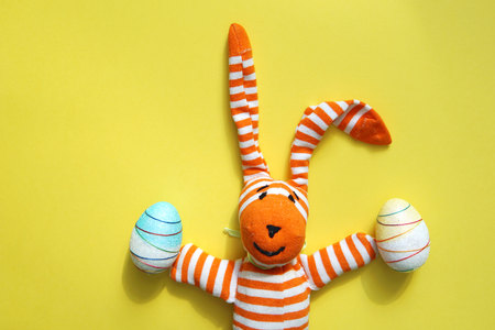 Funny Easter bunny and decorative Easter eggs on yellow background. Copy space.の写真素材