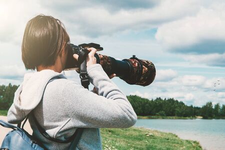 Young woman with a camera with a telephoto lens, photographing birds on the lake. Wildlife...