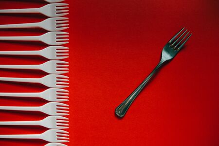 A lot of plastic forks vs a metal one on a red background. The concept of environmental problems,...