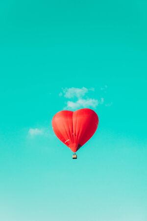 Red balloon in the shape of a heart against the blue sky and some light clouds.の写真素材