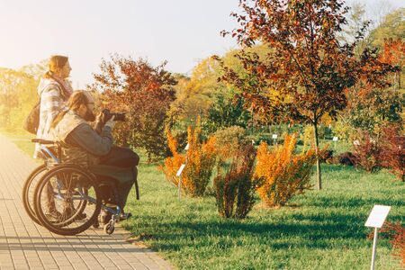 Minsk, Belarus - October 16, 2019. A man taking photo in a wheelchair in a Botanical garden. A woman standing next to him. Concept of happy family with one disabled member.のeditorial素材