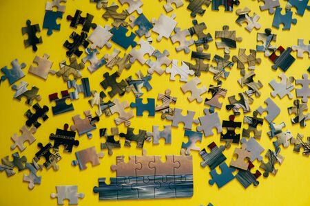 A lot of puzzle pieces on a yellow background. Part of the puzzle is assembled, the rest are waiting in turn.の写真素材