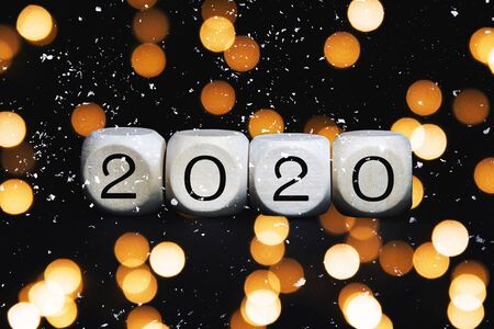 Wooden cubes with 2020 numbers on a black background. Christmas concept greeting card with blurred bokeh lights and snow.の写真素材
