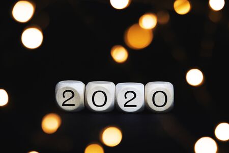 Wooden cubes with 2020 numbers on a black background. Christmas concept greeting card with blurred bokeh lights.の写真素材
