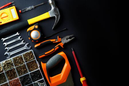 Construction tools for home renovation on black background. Hammer, hand saw, pliers, screwdriver, wrenches, tape measure, multimeter, screws. Maintenance, reparing concept. Place for text, flat lay.の写真素材