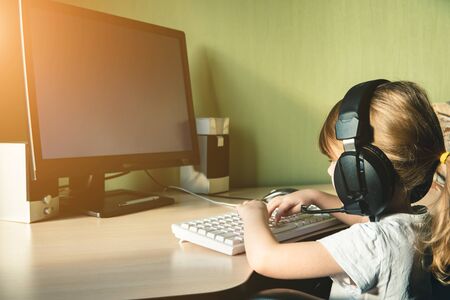 Little girl sitting at the computer with earphones on the head. Freelance, learning at home or...