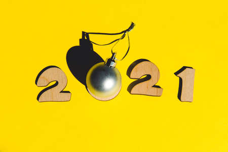 Numbers 2020 from wooden letters and a silver christmas ball on a yellow background. Minimal new year concept.の写真素材