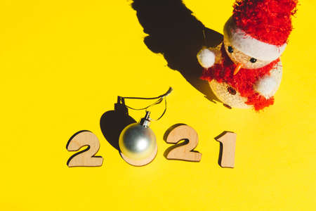 Wooden numbers 2021, little cute snowman and a silver christmas ball on a yellow background. Minimal...