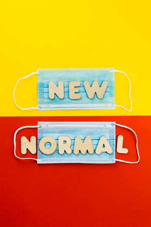 NEW NORMAL words on protective face masks on yellow and red background. Post covid-19 pandemic changes, new reality, wearing face mask in public concept. Copy space, vertical.の写真素材