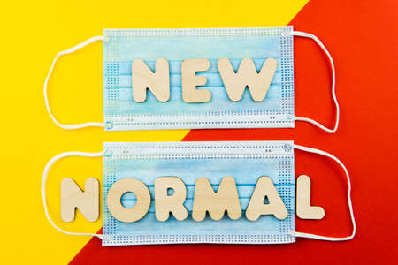 NEW NORMAL words on protective face masks on yellow and red background. Post covid-19 pandemic changes, new reality, wearing face mask in public concept.の写真素材
