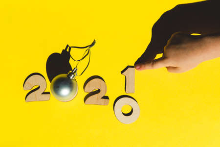 Wooden numbers 2021 chainging 2020 with child hand and a silver christmas ball on a yellow background. Minimal new year concept.の写真素材