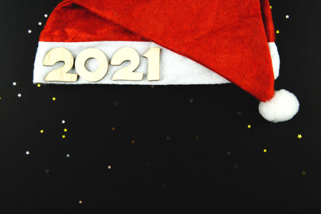 Wooden numbers 2021 on a red Santa hat on a black background with yellow and gray glitter stars.の写真素材