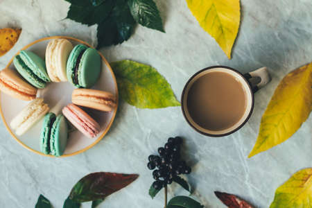 Autumn yellow leaves, a cup of coffee and pastel French macarons cakes on a marble surface. Flat lay composition from above, top view .の写真素材