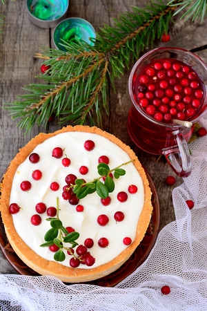 White chocolate cheesecake tart with cranberries with cranberry drink and pine branches and candles on a wooden tableの写真素材