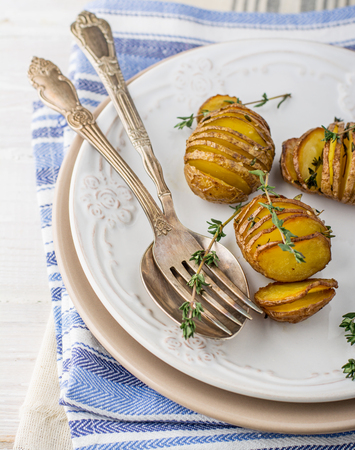 Baked potatoes with thyme accordion and sea salt on the light plate with a spoon. On blue napkin. Selective focus.の写真素材
