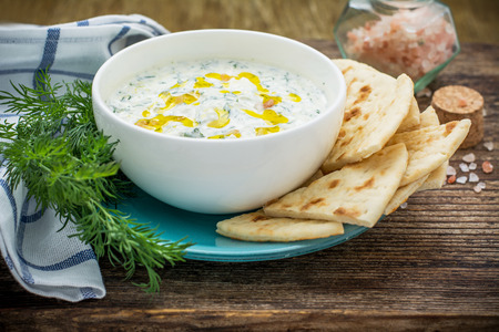 Sauce with yogurt and cucumber for starter with slices of bread on a white plate and a dark natural wood background. selective Focusの写真素材