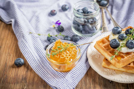 Homemade fresh crispy waffles for breakfast with fresh blueberries and honey on a ceramic bowl and a wooden background. selective Focusの写真素材