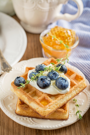 Homemade fresh crispy waffles for breakfast with fresh blueberries and honey on a ceramic bowl and a wooden background. selective Focusの写真素材