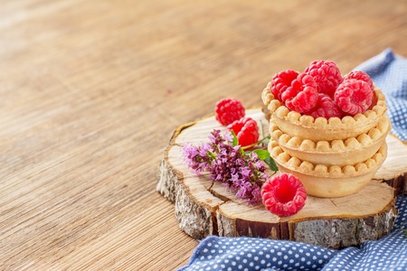 Tartlets of pastry filled with fresh garden raspberries with a sprig of oregano on a wooden dark background. selective Focusの写真素材