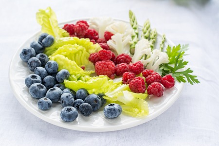 Assorted salad with blueberries, raspberries, asparagus, cauliflower, lettuce leaves on a white plate on a light background. selective Focusの写真素材