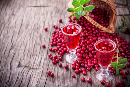 Sweet cranberry liqueur in two glasses on the background of ripe berries on a dark wooden background. selective Focusの写真素材