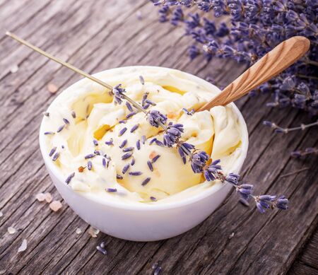 Herbal butter for breakfast with lavender flowers in a white ceramic cup with a wooden spoon on the wooden background with a bouquet of fragrant cut lavandly. selective Focusの写真素材