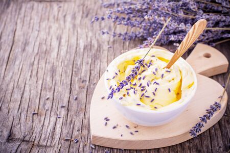 Herbal butter for breakfast with lavender flowers in a white ceramic cup with a wooden spoon on the wooden background with a bouquet of fragrant cut lavandly. selective Focusの写真素材