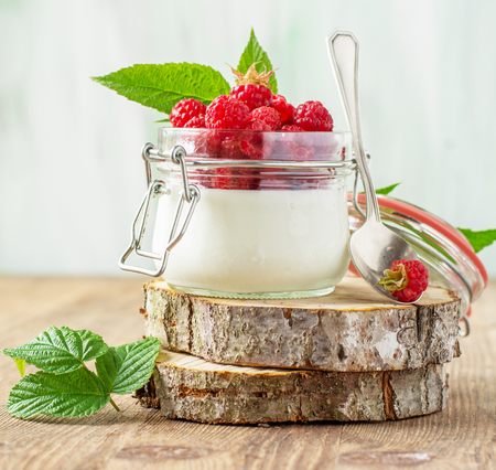 Jar of fresh homemade yogurt with fresh raspberries ripe for breakfast on a wooden background. The concept of healthy natural foods. selective Focusの写真素材