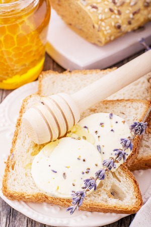 Appetizing sandwich with fresh homemade butter with lavender flowers and flower honey with a spoon on a wooden background. The concept of natural organic food. selective Focusの写真素材