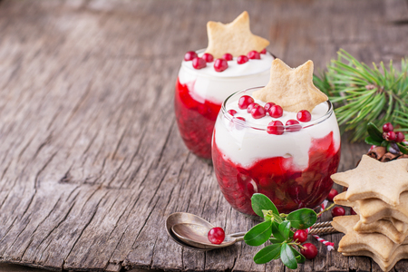 Dessert with cranberry sauce and sour cream decorated gingerbread cookies in the shape of stars and fresh berries cranberries in glasses on dark wooden background. selective Focus