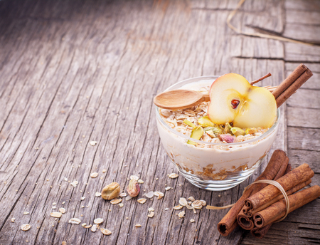 Overnight Oatmeal with yogurt, ground cinnamon and slice of apple in a glass bowl on a wooden background with honey, pistachios, cinnamon and apple. The concept of healthy food. selective Focusの写真素材