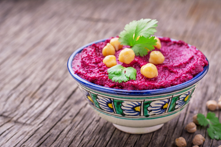 Beetroot hummus with chickpeas and cilantro sprigs in a blue painted bowl on dark wooden background. selective Focusの写真素材