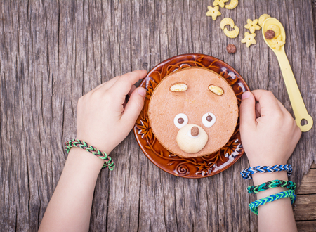 Homemade chocolate cake for breakfast in the form of the muzzle bear on the ceramic plate in the hands of a child. Top view. selective Focusの写真素材