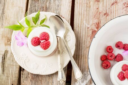 Homemade fresh yogurt with fresh raspberries for breakfast portioned cups on a wooden background.