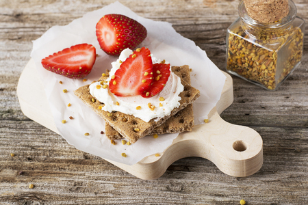 Crispy bread for breakfast for a healthy diet with curd cheese, strawberry, flower bee pollen on a wooden cutting board easy. concept of healthy family nutrition. selective Focusの写真素材