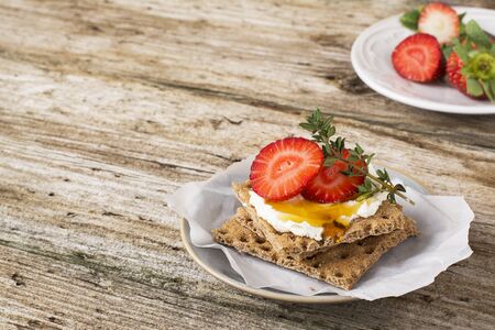 Healthy and tasty breakfast cereal crispy bread roll with curd cheese, strawberries, honey and thyme on a wooden tableの写真素材