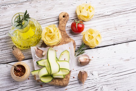 Ingredients for cooking pasta with vegetables - spaghetti, zucchini, tomatoes, garlic, rosemary, pepper. The concept of simple home cooking with natural products. Selective focusの写真素材