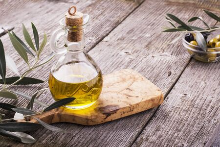 Jug with extra virgin olive oil on olive cutting board surrounded by branches of the olive tree and olives. Selective focus. The concept of a healthy natural foodの写真素材